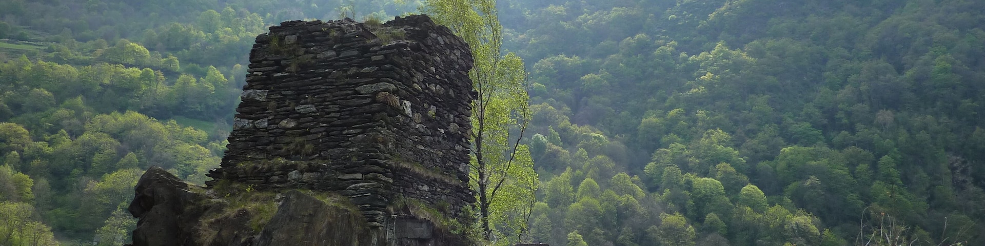 A stone ruin with inscriptions, surrounded by lush green hills and a clear sky.