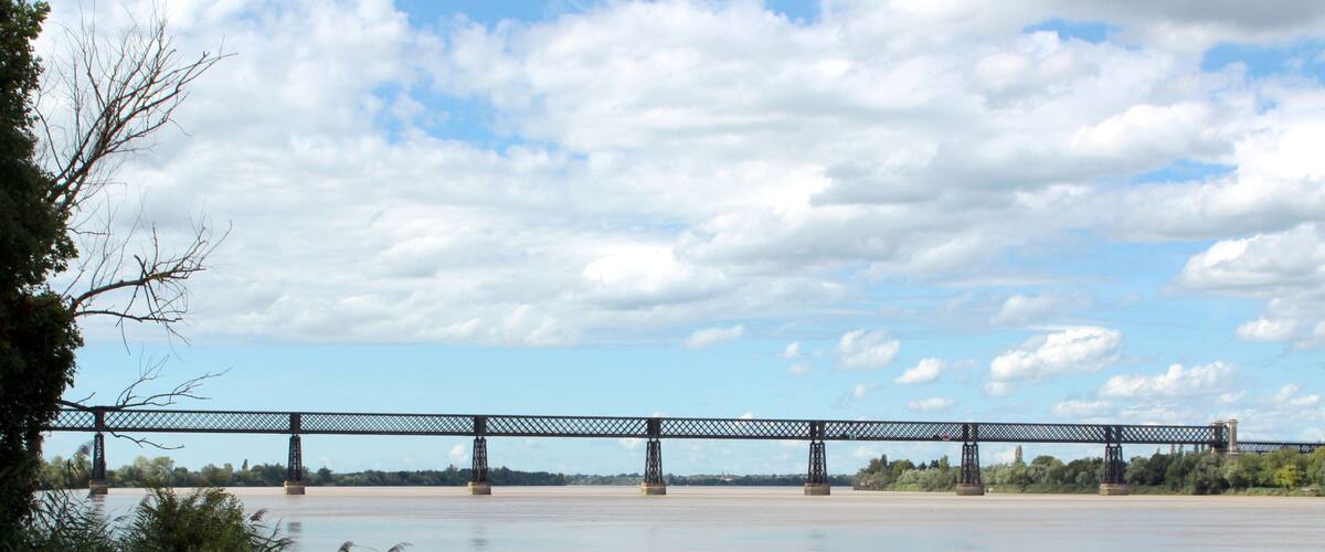 A large metal bridge spanning a wide river with a cloudy sky above.
