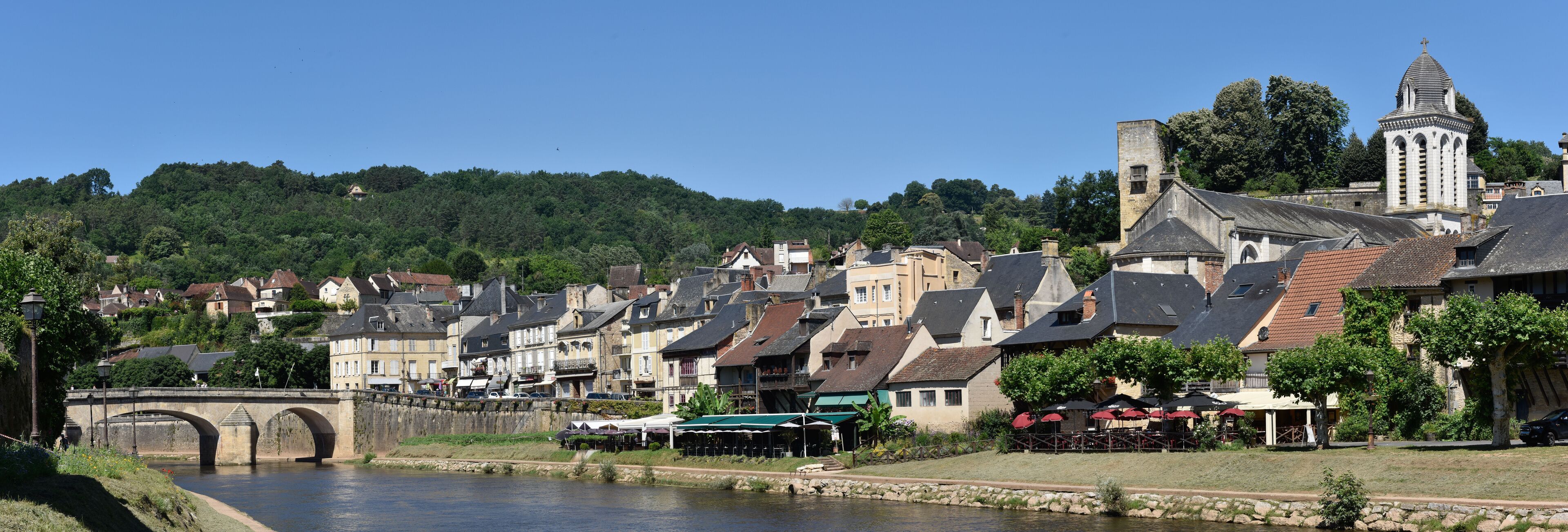 A riverside town with historic buildings, a stone bridge, and a church tower.
