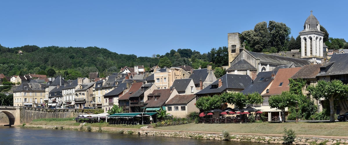 A riverside town with historic buildings, a stone bridge, and a church tower.