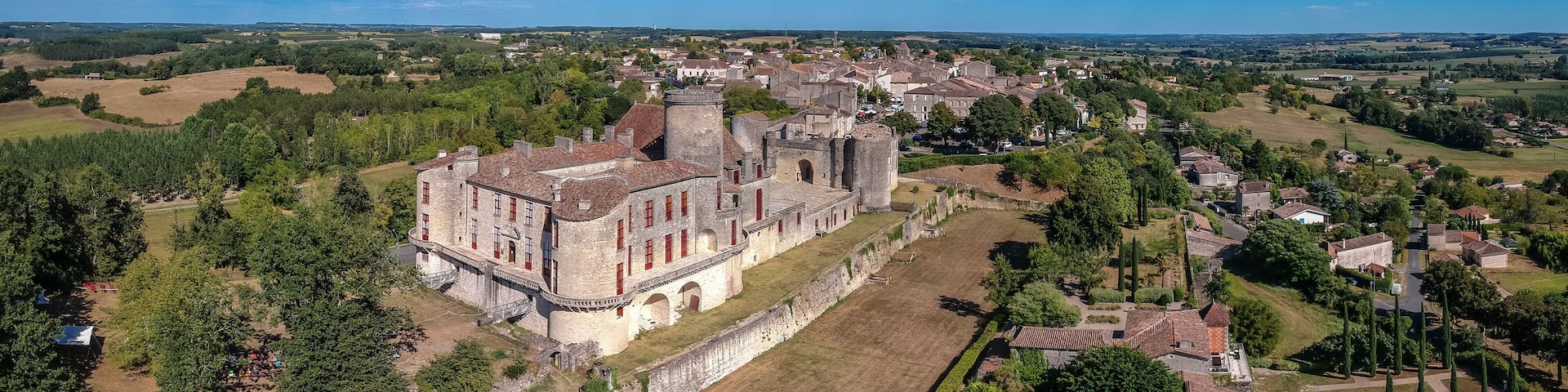 An aerial view of a historic castle surrounded by lush greenery and a small village.