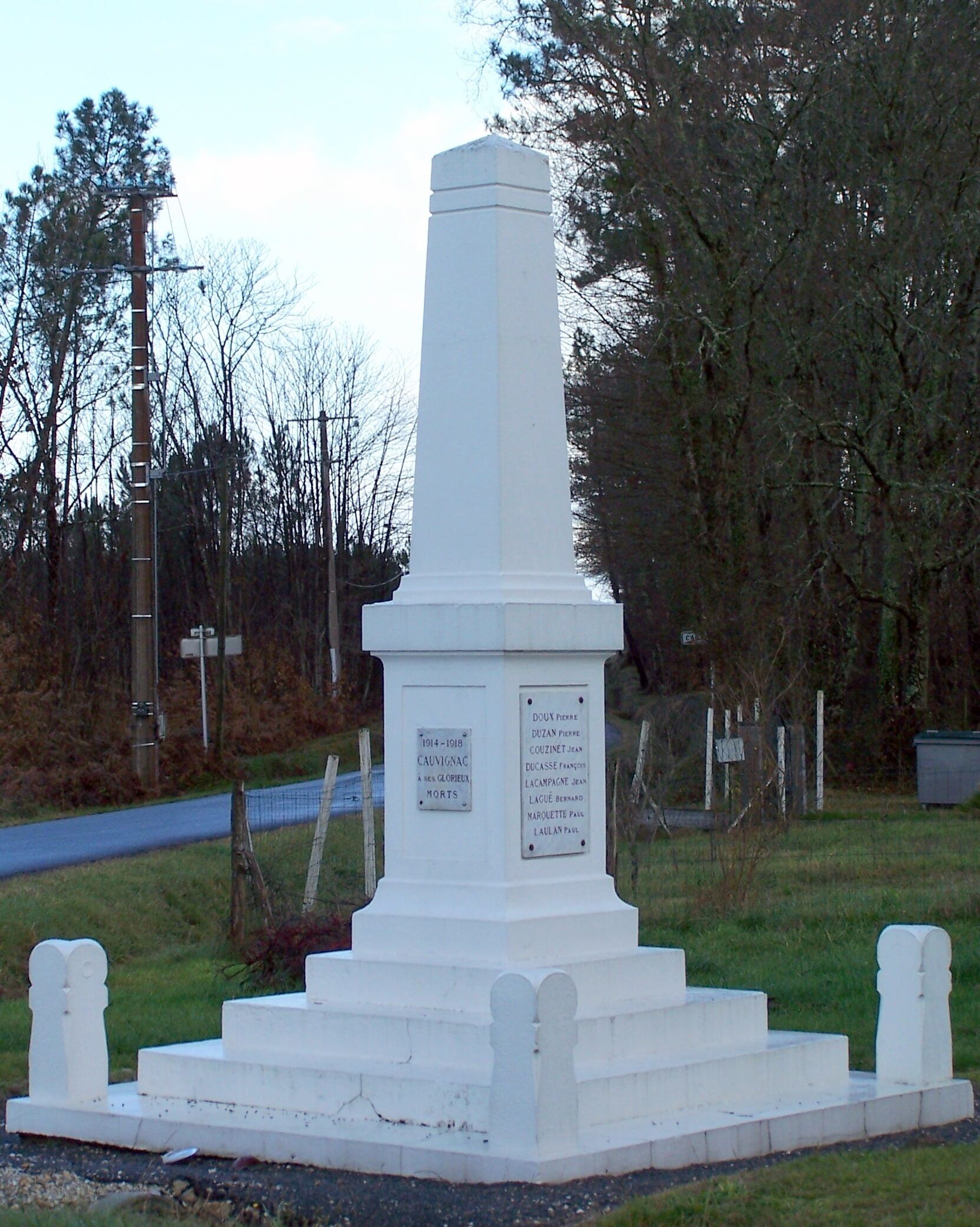 A white monument with inscriptions, surrounded by grass and trees.