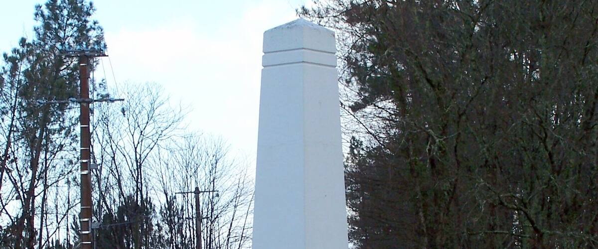 A white monument with inscriptions, surrounded by grass and trees.