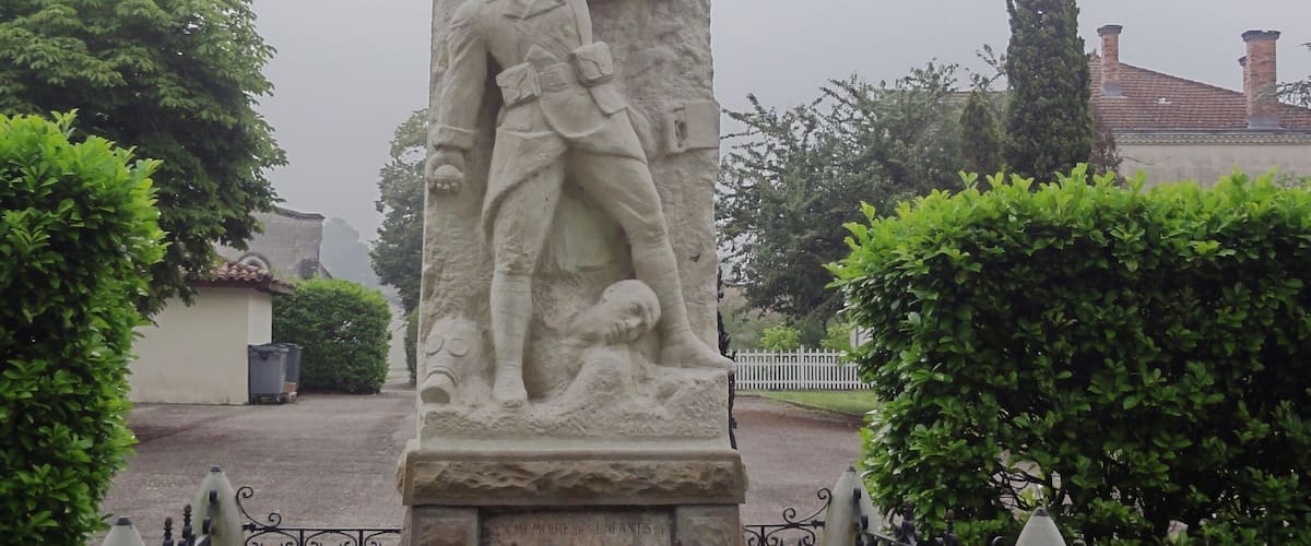 A stone monument with a soldier and a fallen comrade, surrounded by a fence and greenery.