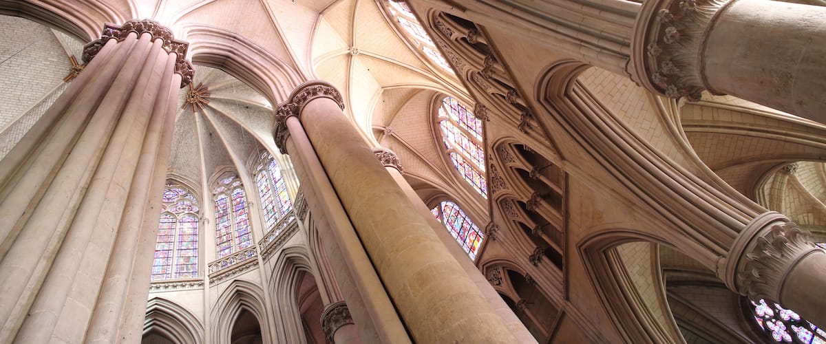 A cathedral interior with high vaulted ceilings, large stained glass windows, and ornate columns.
