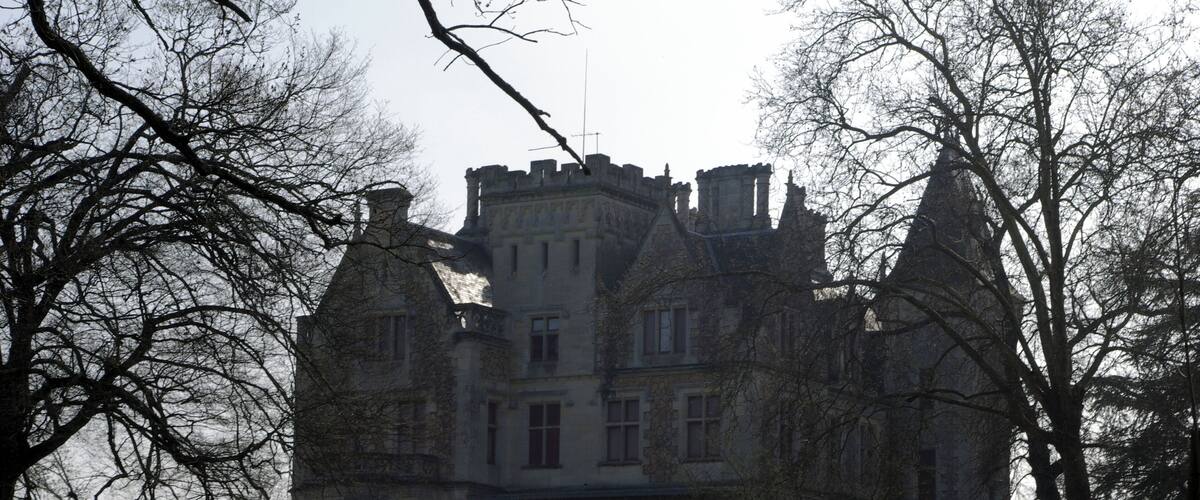 A large, historic castle with multiple towers and turrets, surrounded by a well-maintained lawn and leafless trees.
