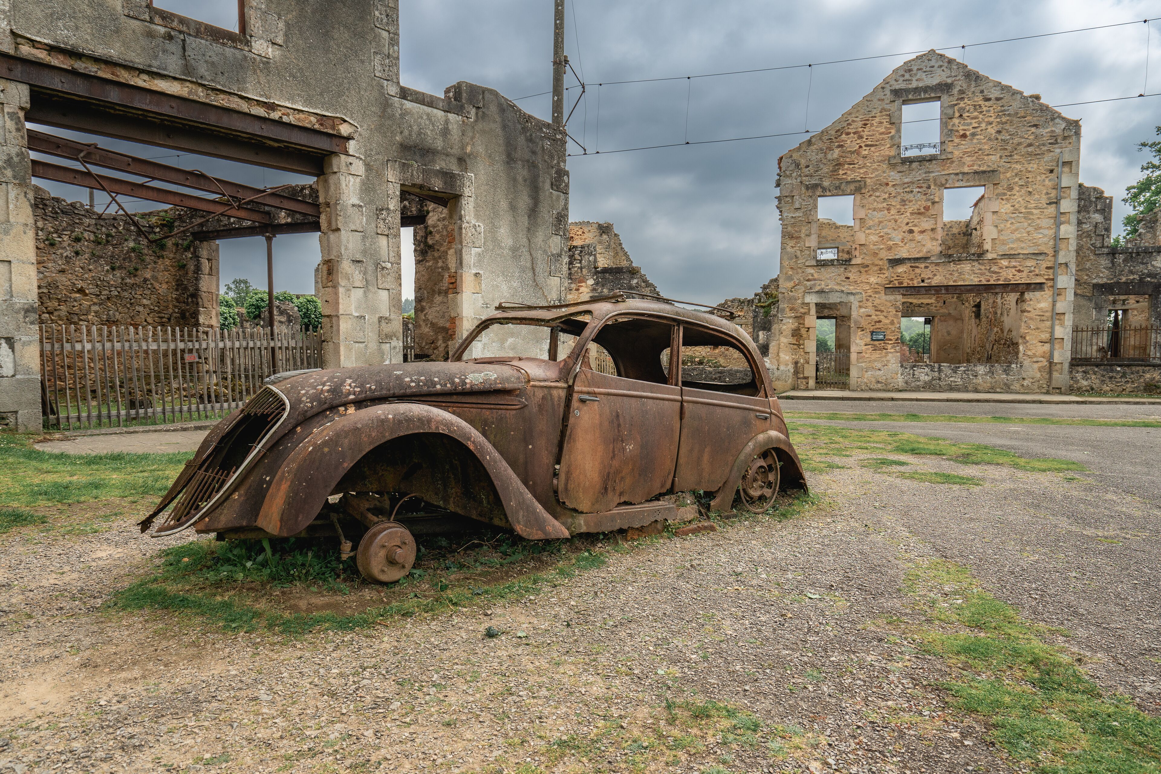 An old, rusted car parked in front of a dilapidated stone building.