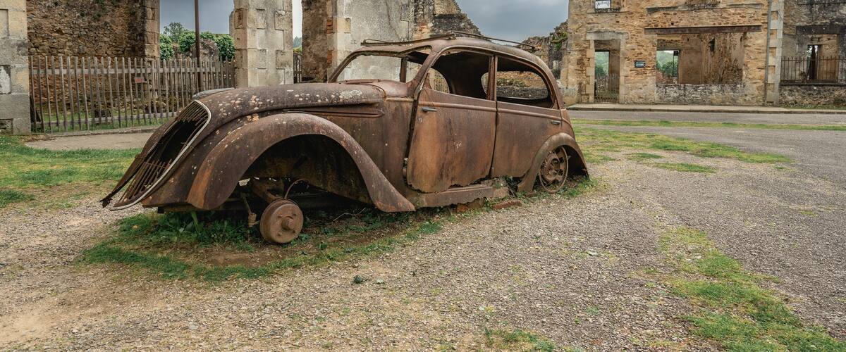 An old, rusted car parked in front of a dilapidated stone building.