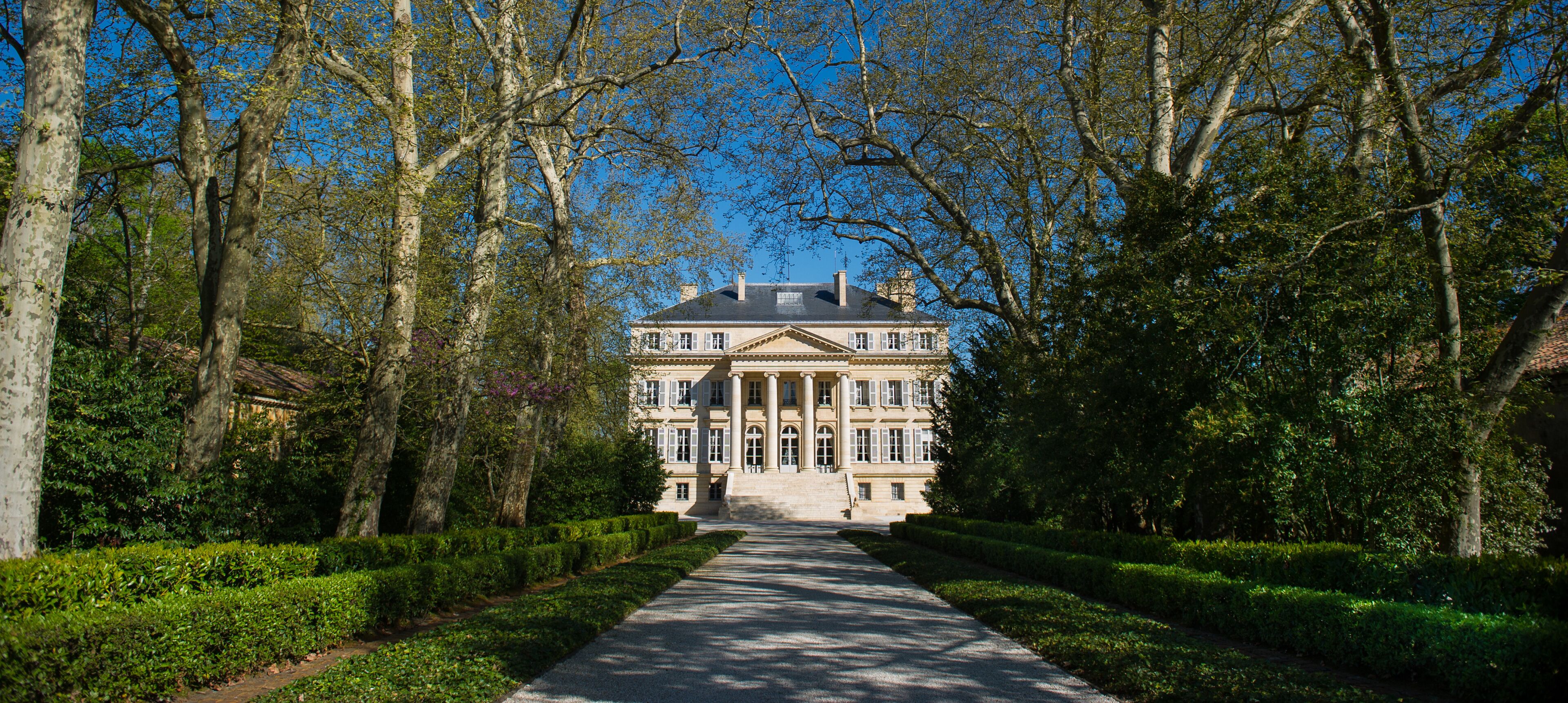 A grand mansion with a symmetrical facade, surrounded by a well-manicured garden and tall trees.