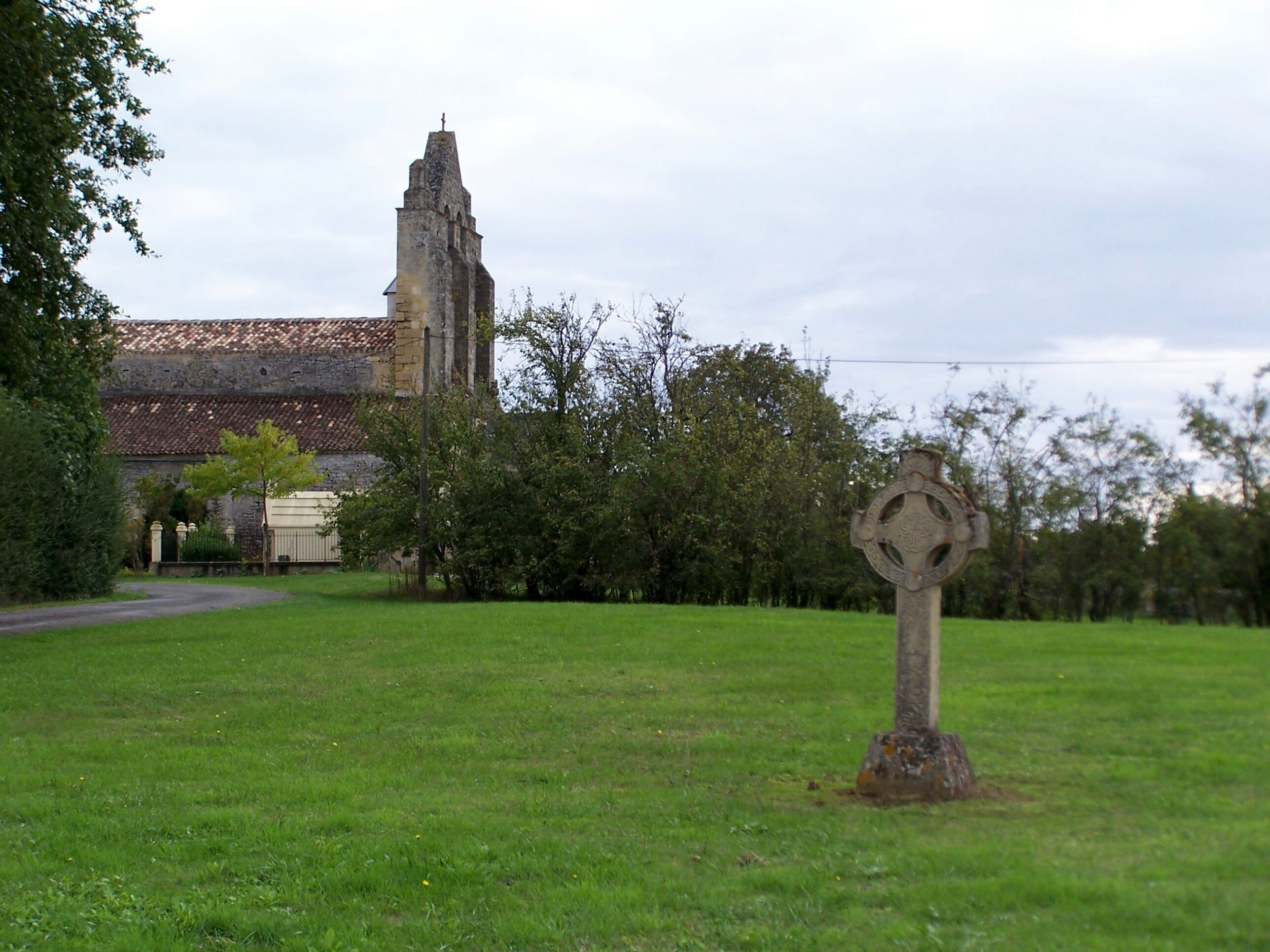 A grassy field with a stone cross and a church with a tower in the background.