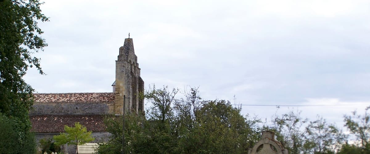 A grassy field with a stone cross and a church with a tower in the background.