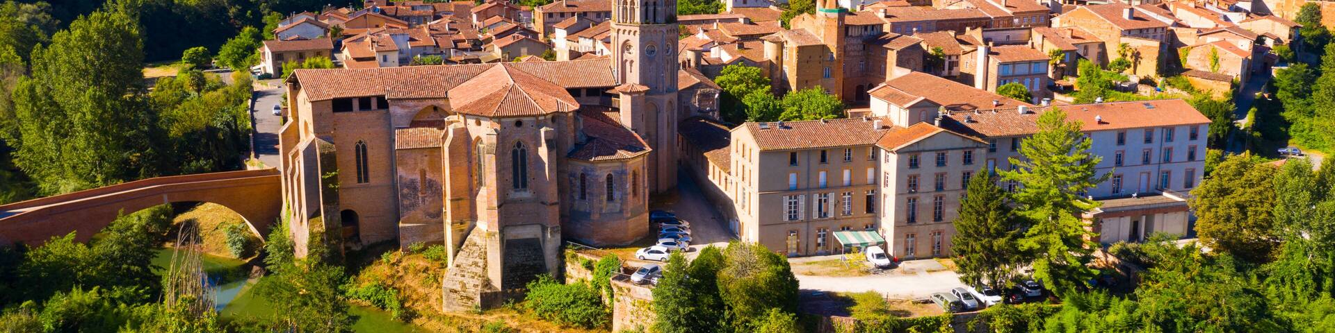 Scenic aerial view of Rieux-Volvestre town on banks of small tributary of Garonne in summer overlooking ancient Roman Catholic Cathedral, France