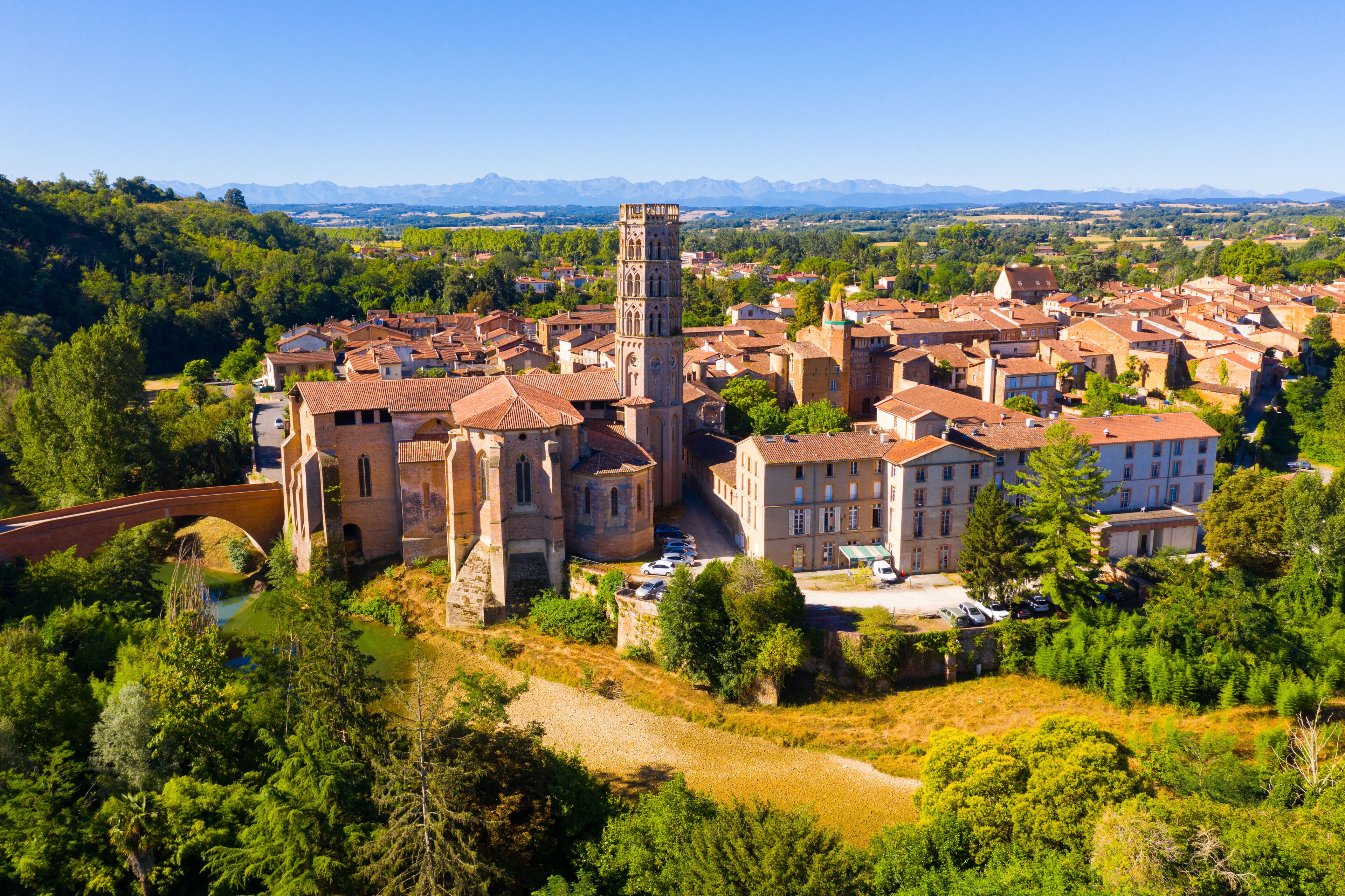 A historic town with a prominent church featuring a tall bell tower, surrounded by lush greenery and rolling hills in the background.