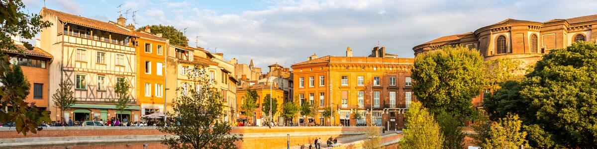 A historic European town with a river, traditional buildings, and a prominent round building.