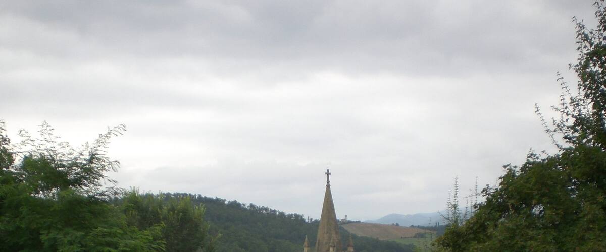 A church with a tall steeple and a clock tower, surrounded by lush greenery and a grassy path.