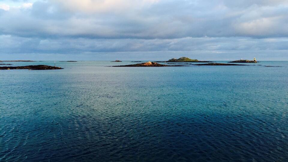 A calm sea with several small islands and a lighthouse in the distance.