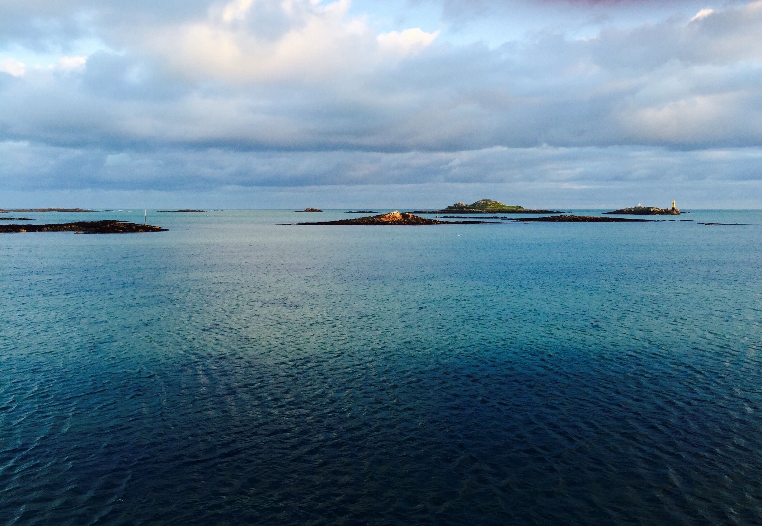A calm sea with several small islands and a lighthouse in the distance.