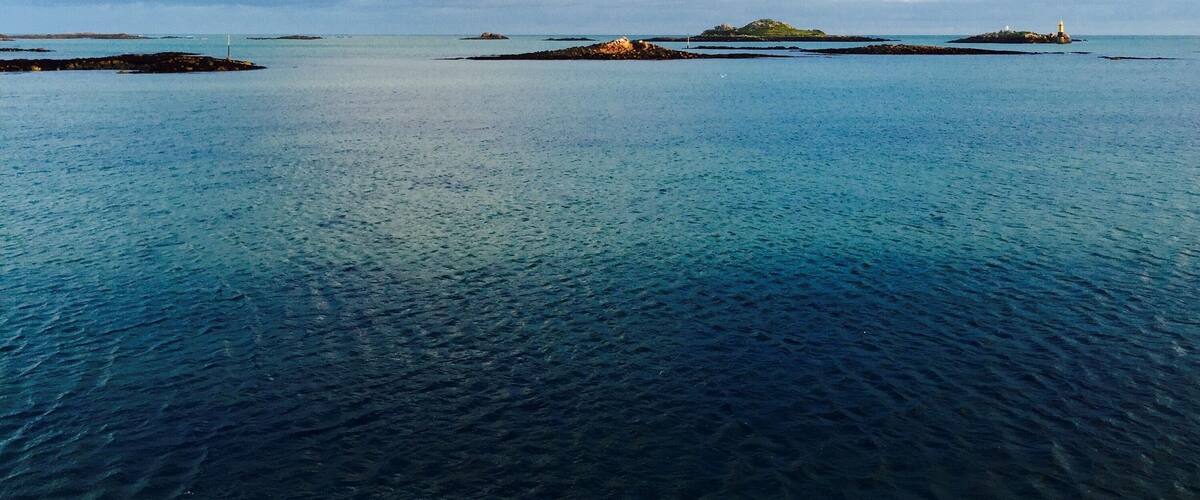 A calm sea with several small islands and a lighthouse in the distance.