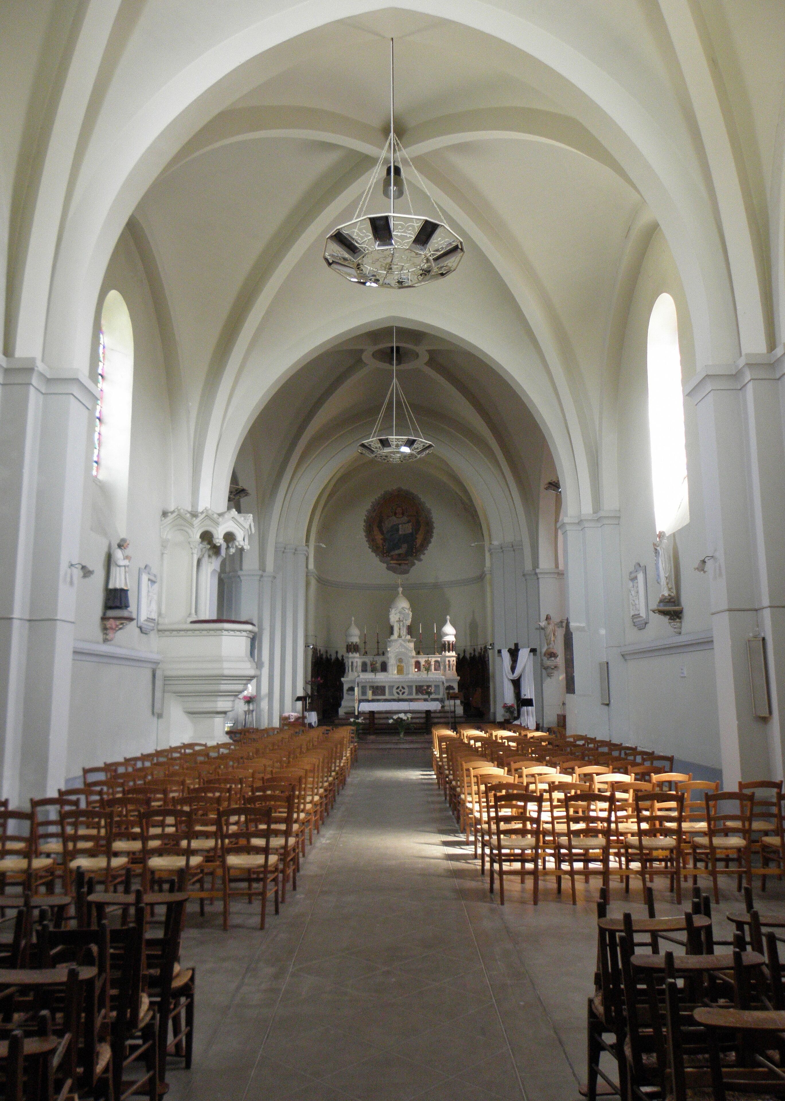 A church interior with wooden pews, a central altar, and a large chandelier.