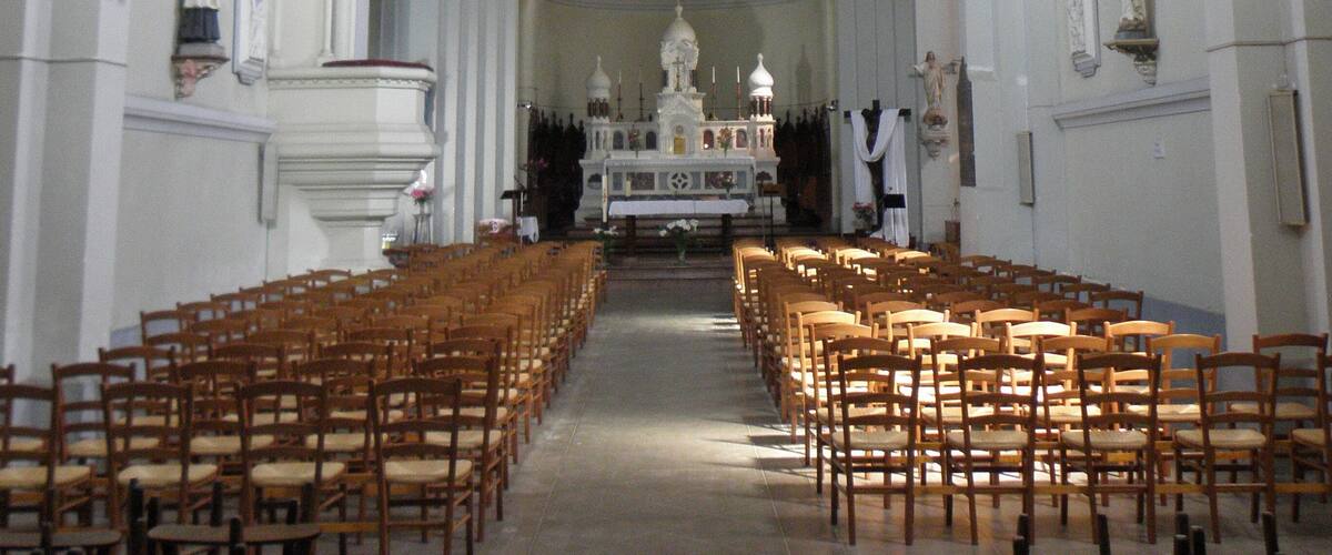 A church interior with wooden pews, a central altar, and a large chandelier.