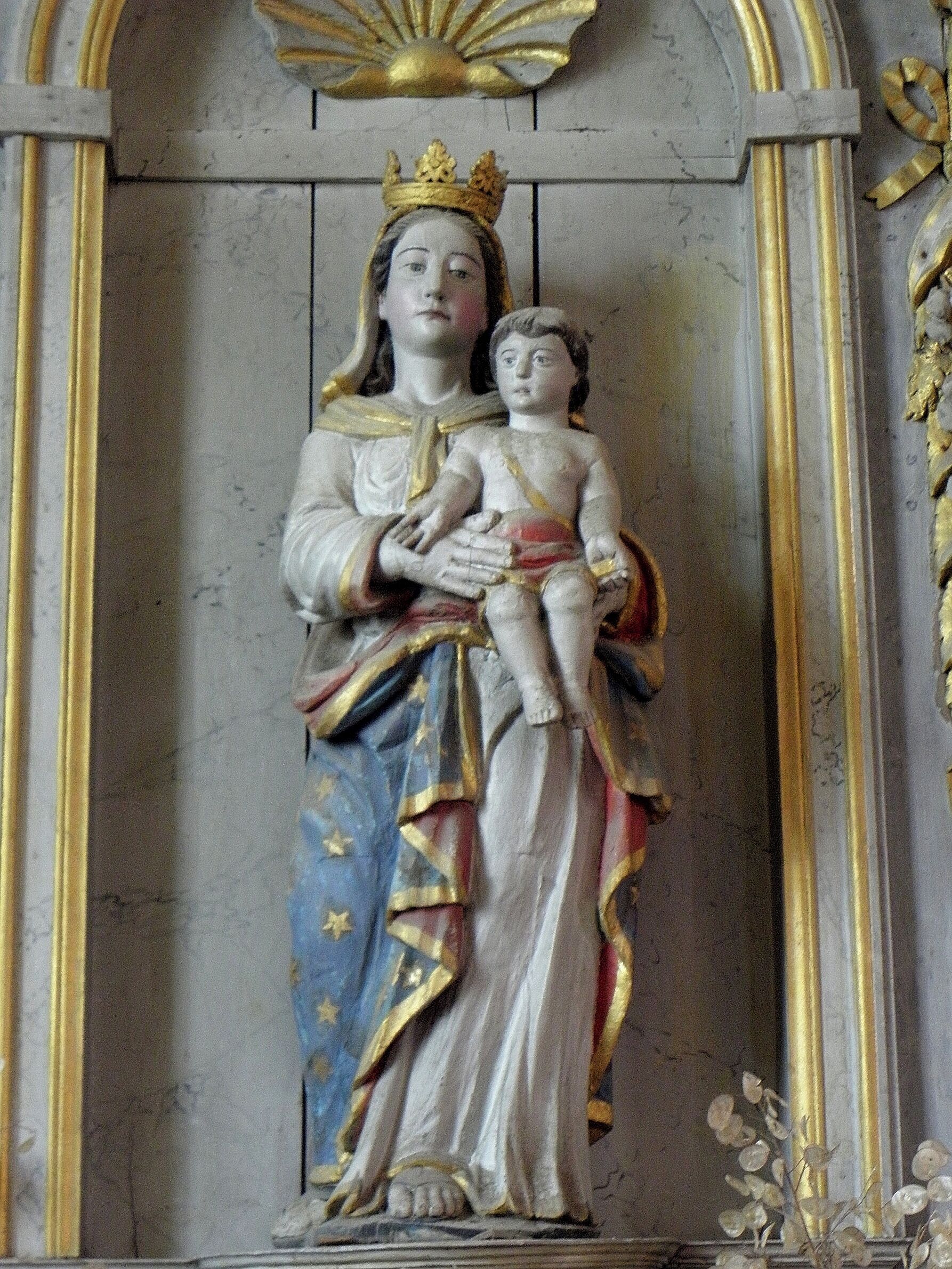 A statue of a crowned figure holding a child, set against a marble background with gold accents.