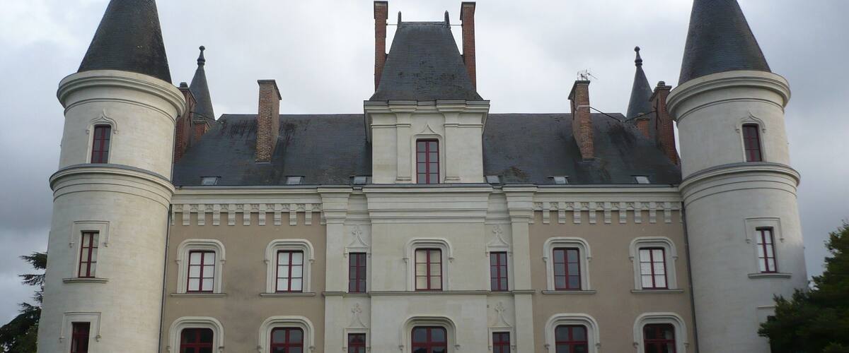 A large, historic building with two prominent towers and a central section with multiple windows.
