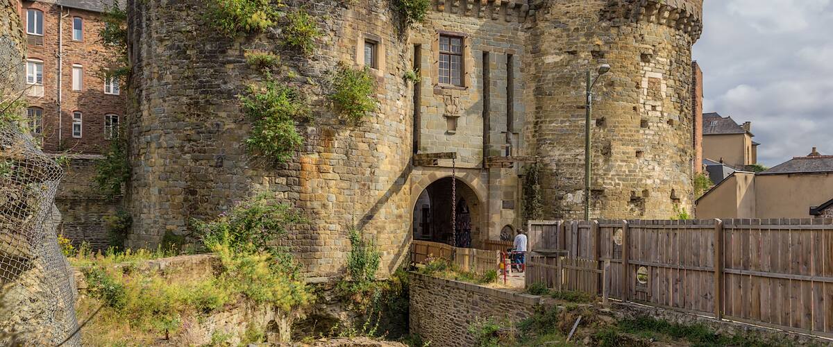 A historic stone castle with a round tower, arched entrance, and a wooden fence.