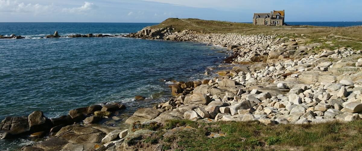 A rocky coastline with a stone house on a hill.