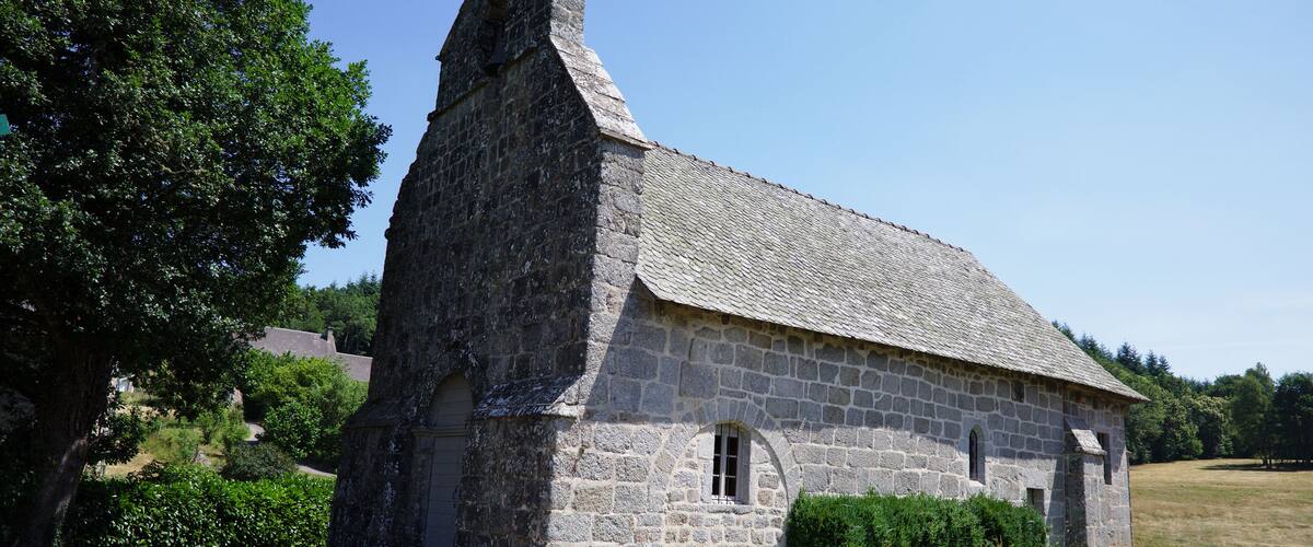 A stone church with a steep roof and a bell tower, surrounded by a grassy field and trees.