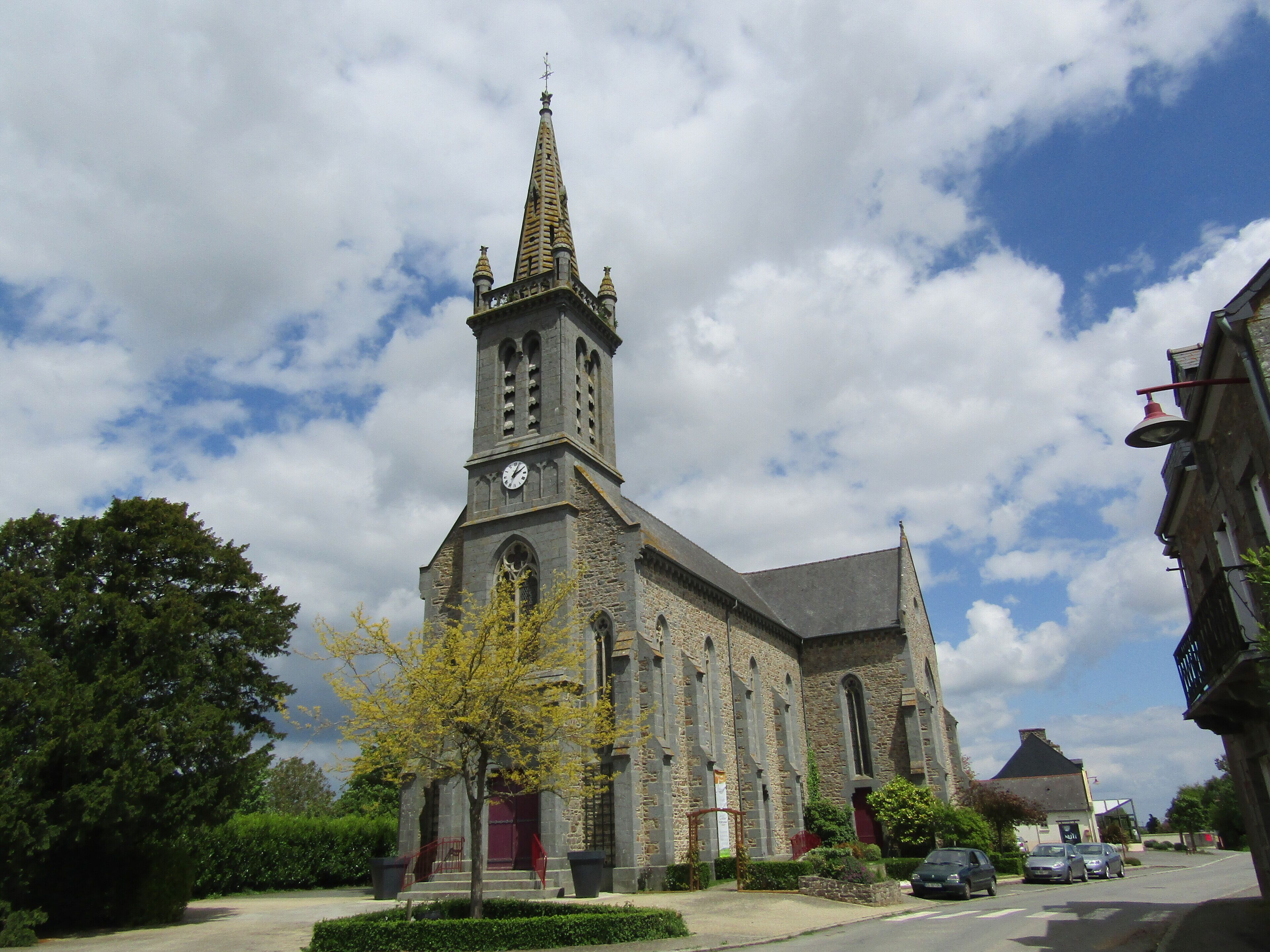 A historic church with a tall spire and clock tower, surrounded by trees and parked cars.