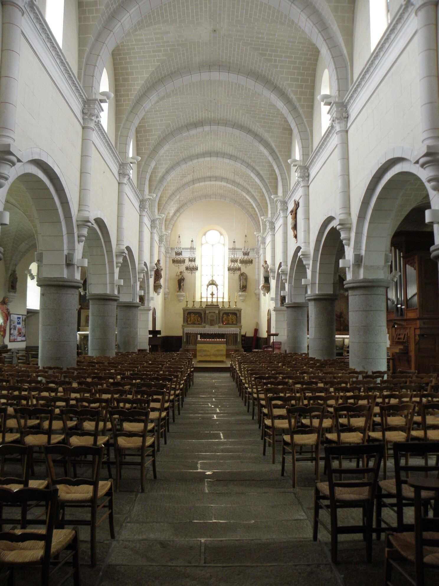 An interior of a church with rows of wooden pews, white brick arches, and a central altar.