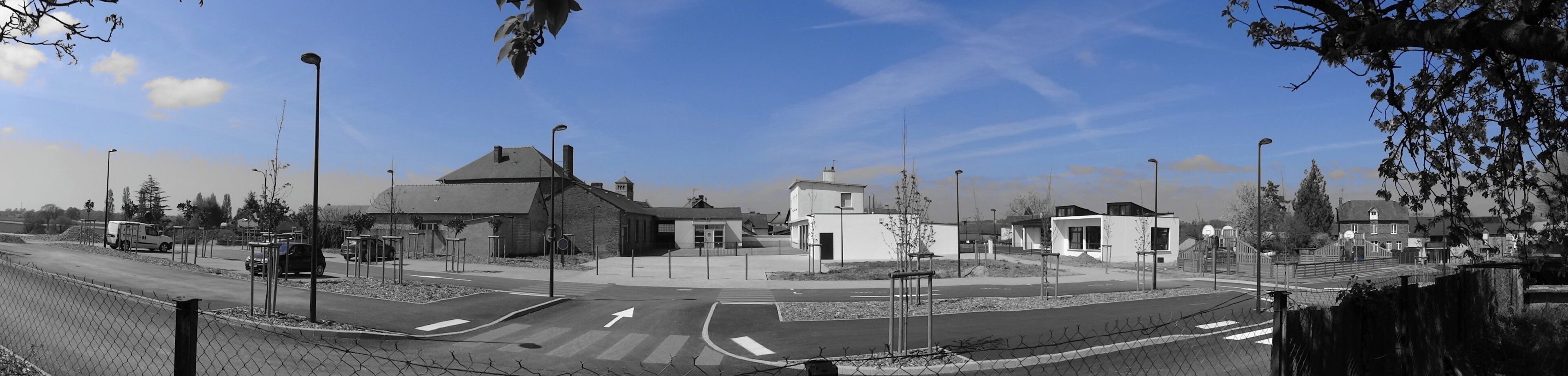 A roundabout with modern buildings, a clear sky, and a fence along the road.