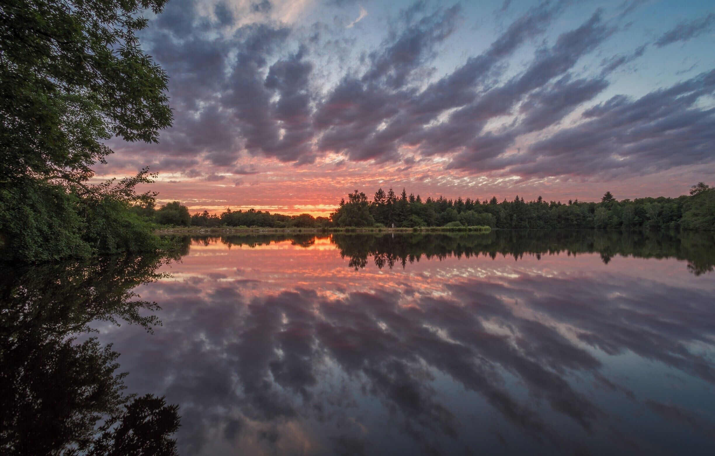 A calm lake reflecting a sunset sky with clouds.