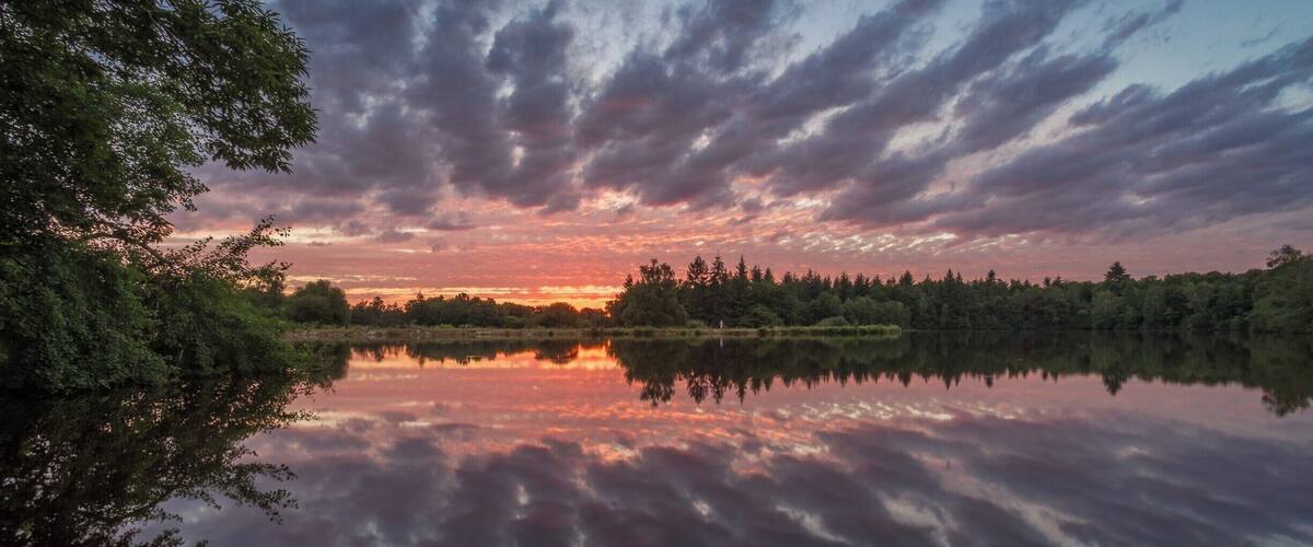 A calm lake reflecting a sunset sky with clouds.