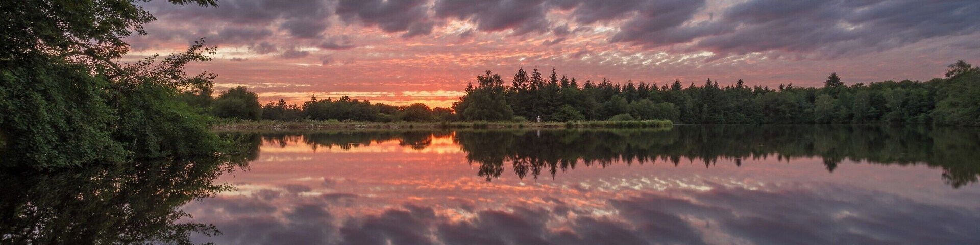 A calm lake reflecting a sunset sky with clouds.