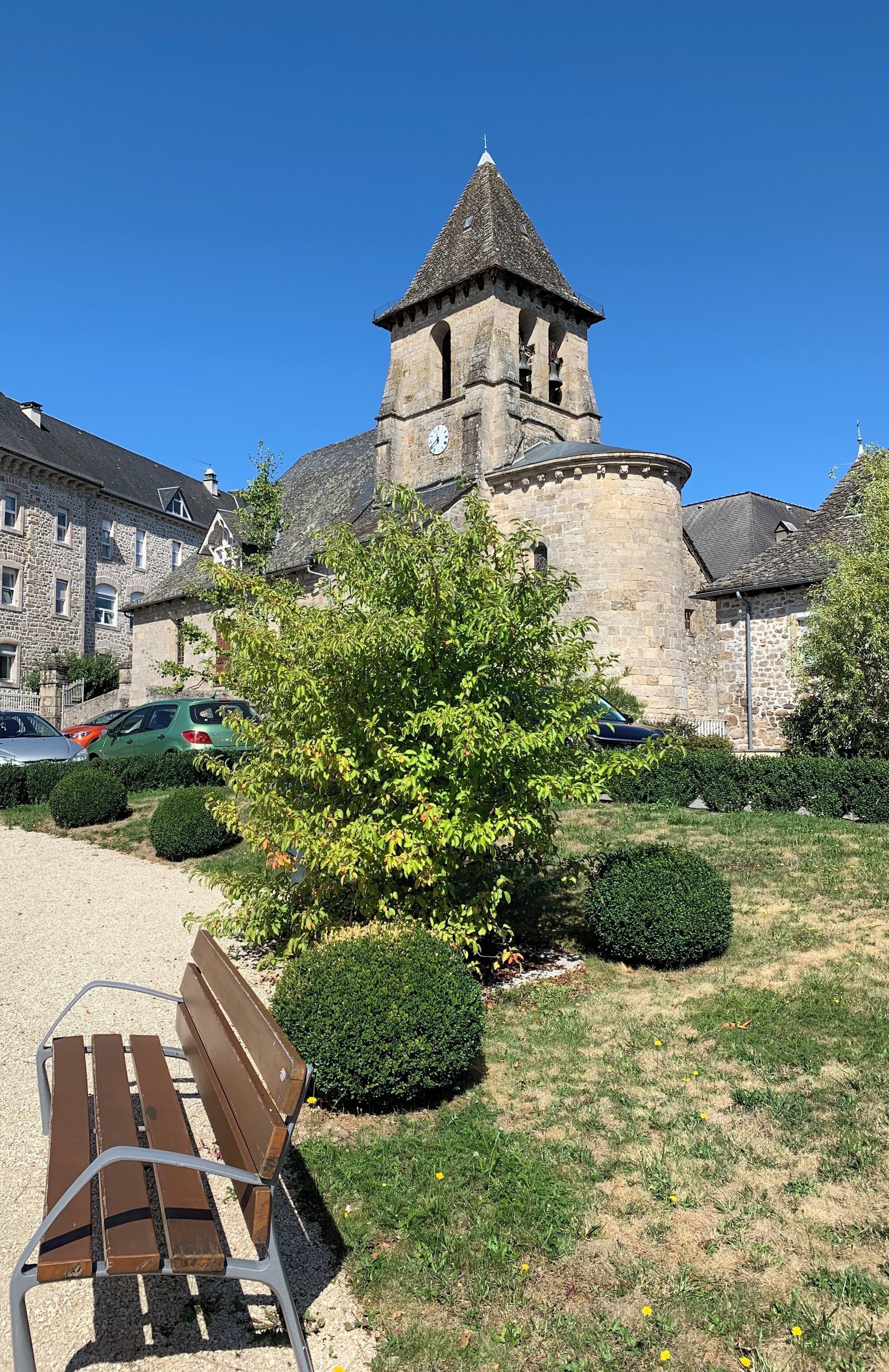 A stone tower with a clock, surrounded by neatly trimmed bushes and a bench.