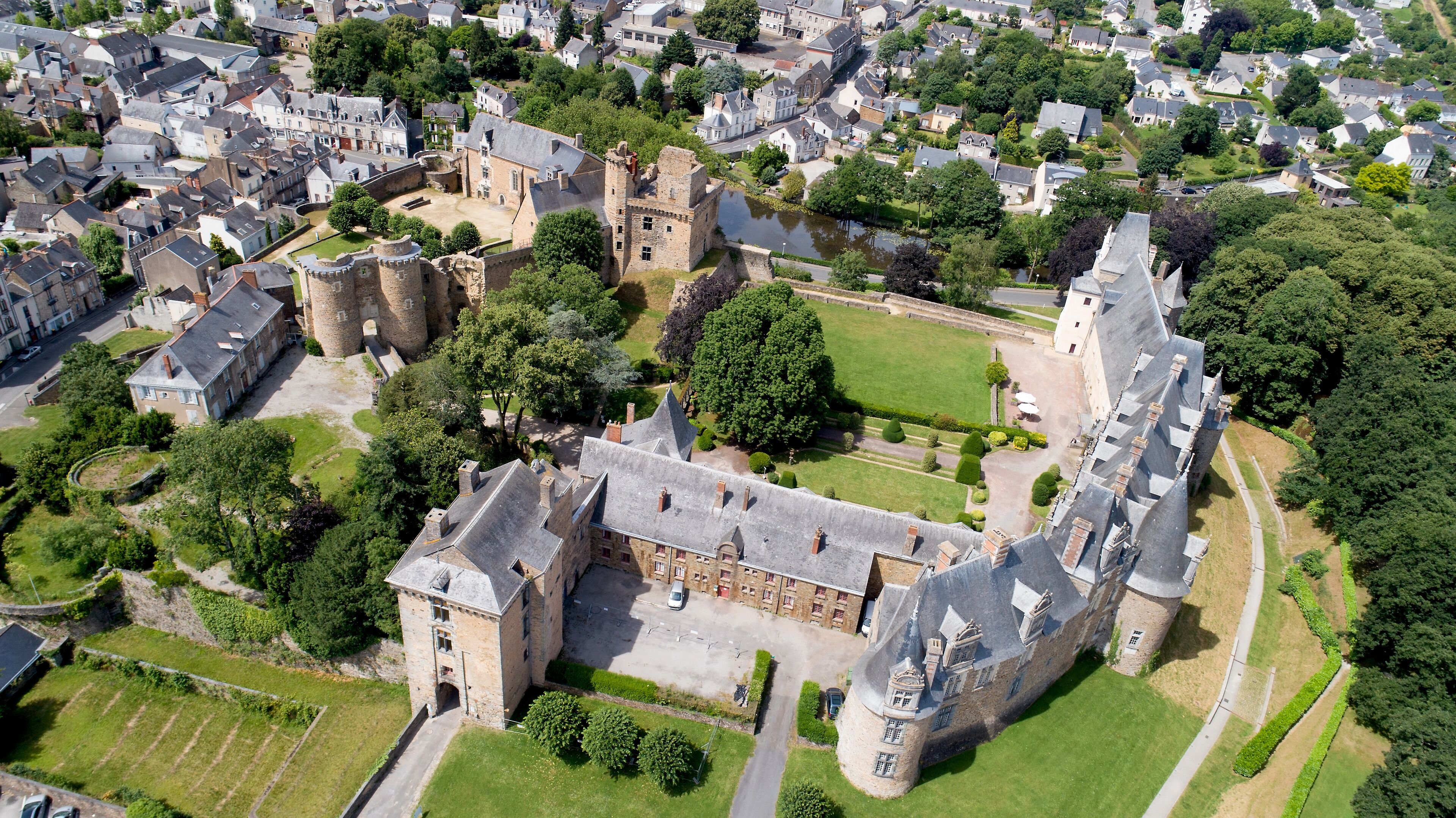 An aerial view of a historic castle surrounded by lush greenery and residential buildings.