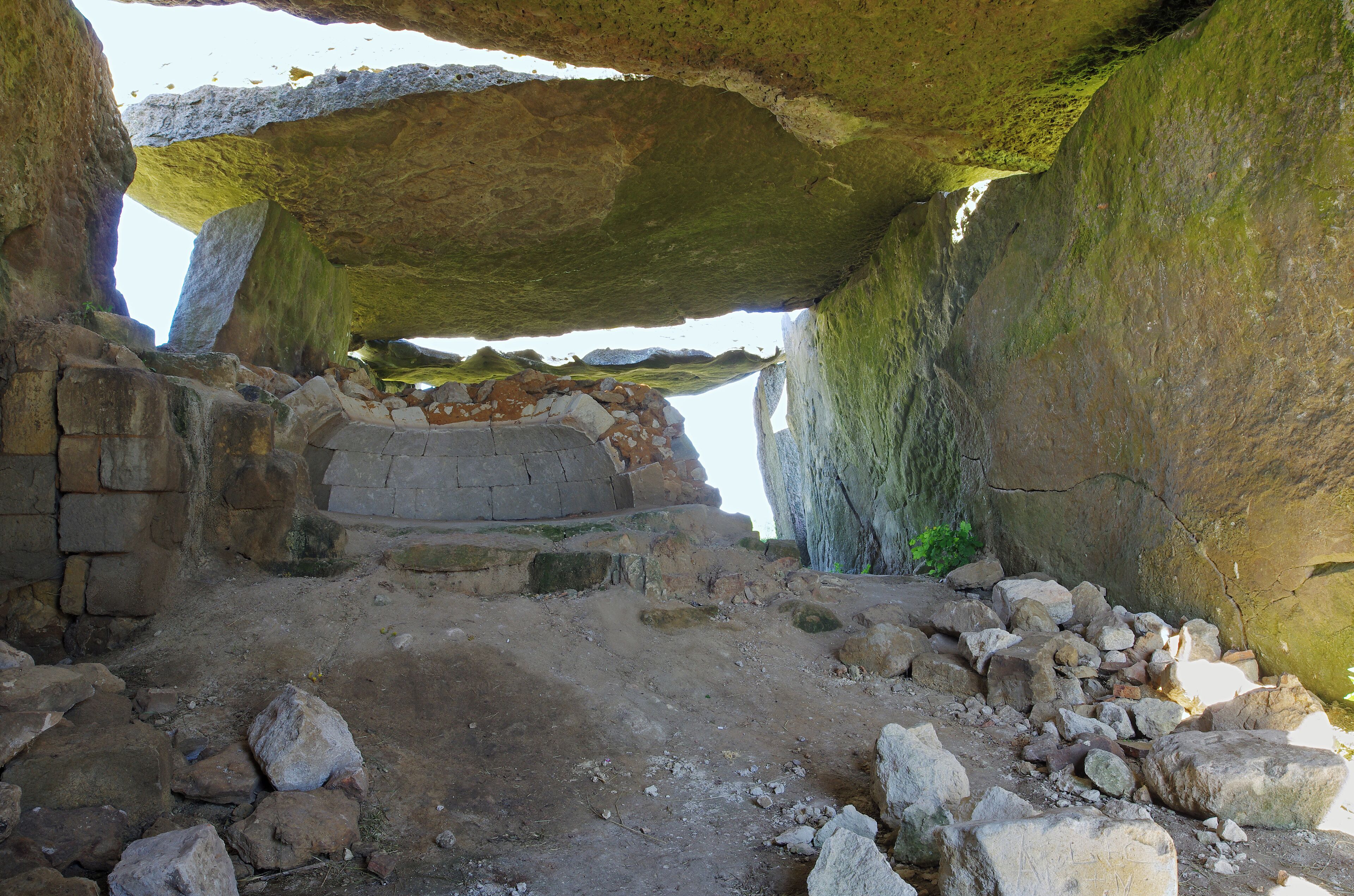 An ancient stone structure with large rock formations and a partially collapsed wall.