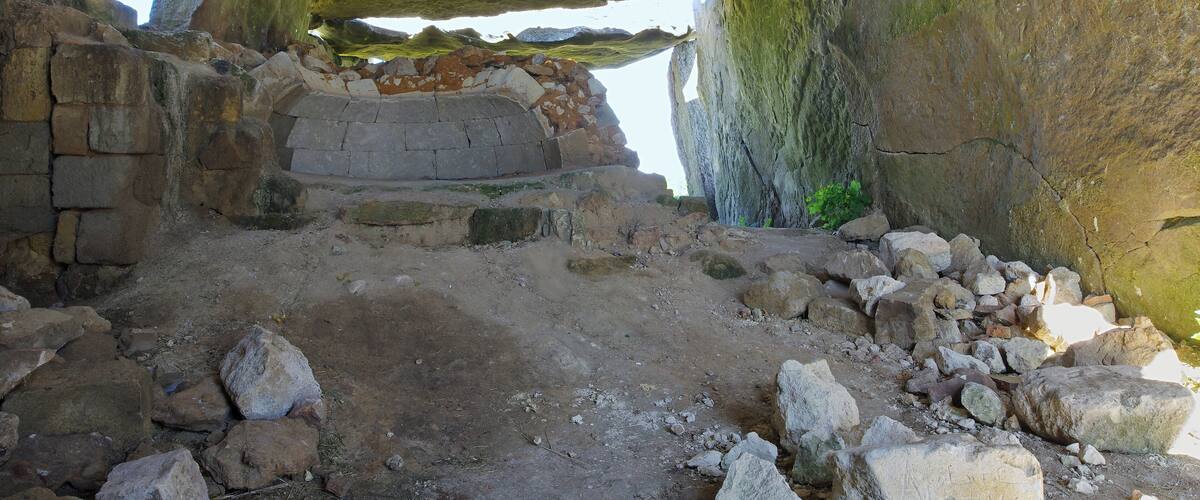 An ancient stone structure with large rock formations and a partially collapsed wall.