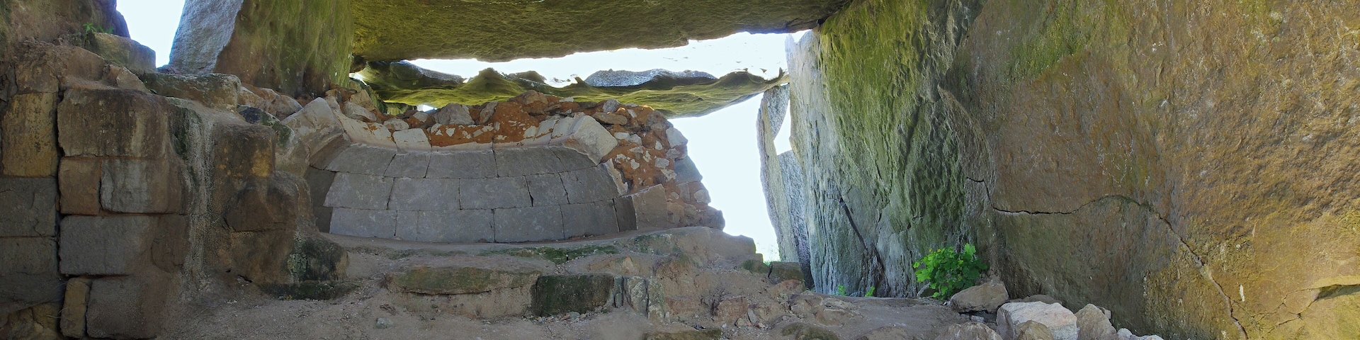 An ancient stone structure with large rock formations and a partially collapsed wall.