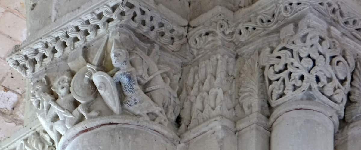 A detailed stone column with intricate carvings and a small figure holding a shield.