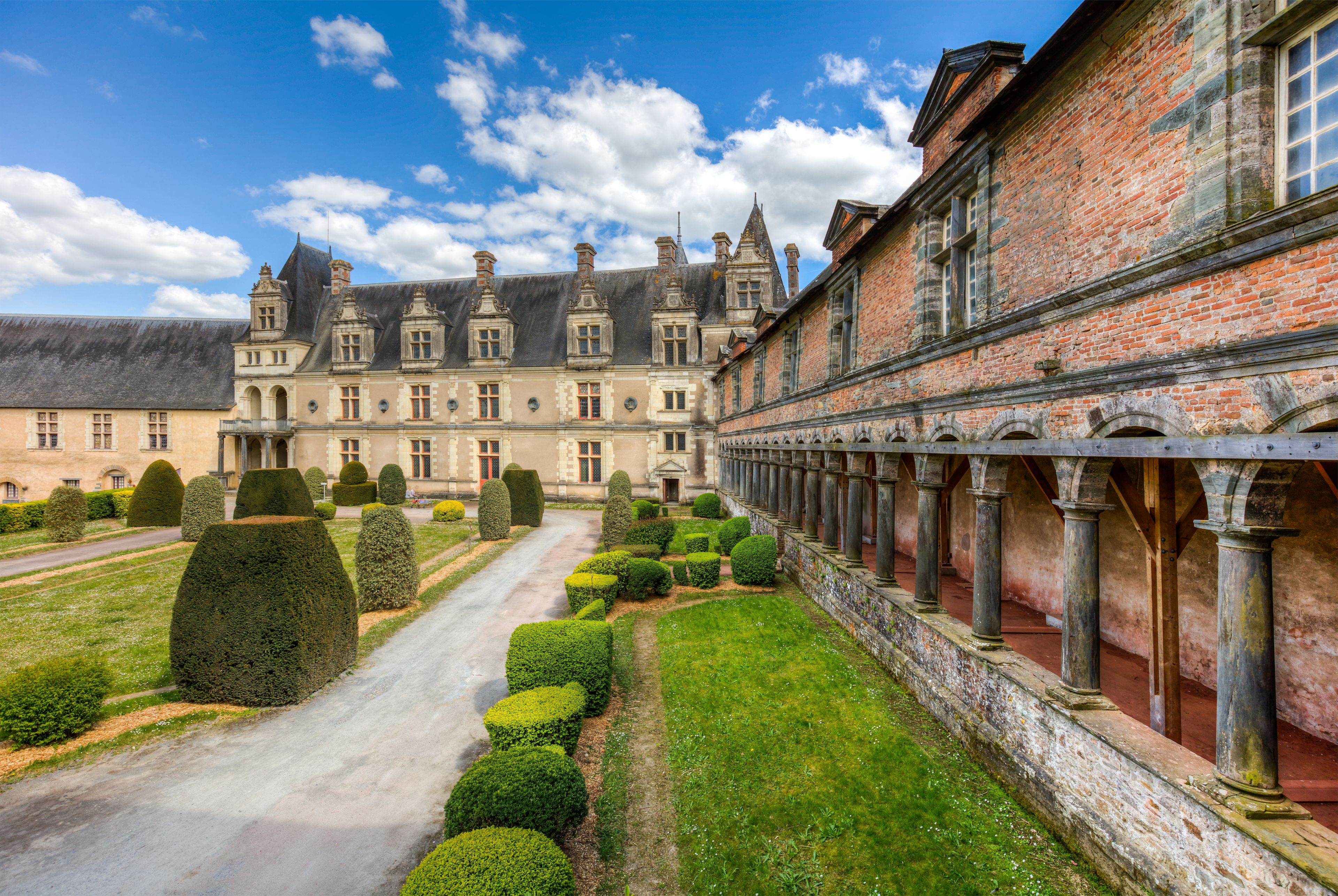 A historic building with a long corridor and neatly trimmed hedges.