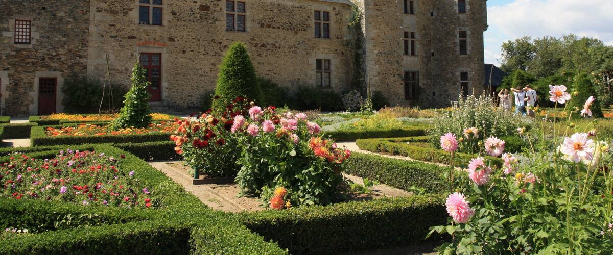 A historic stone castle with a garden featuring pink and red flowers.