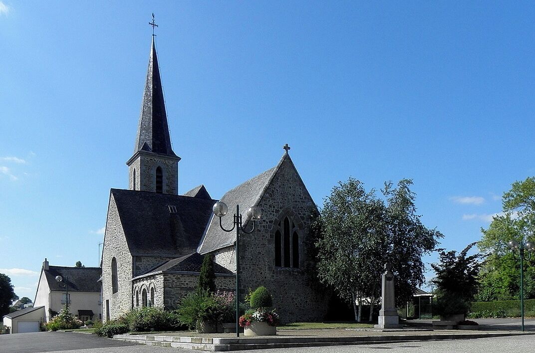 A church with a tall steeple and a cross on top, surrounded by greenery and a clear blue sky.
