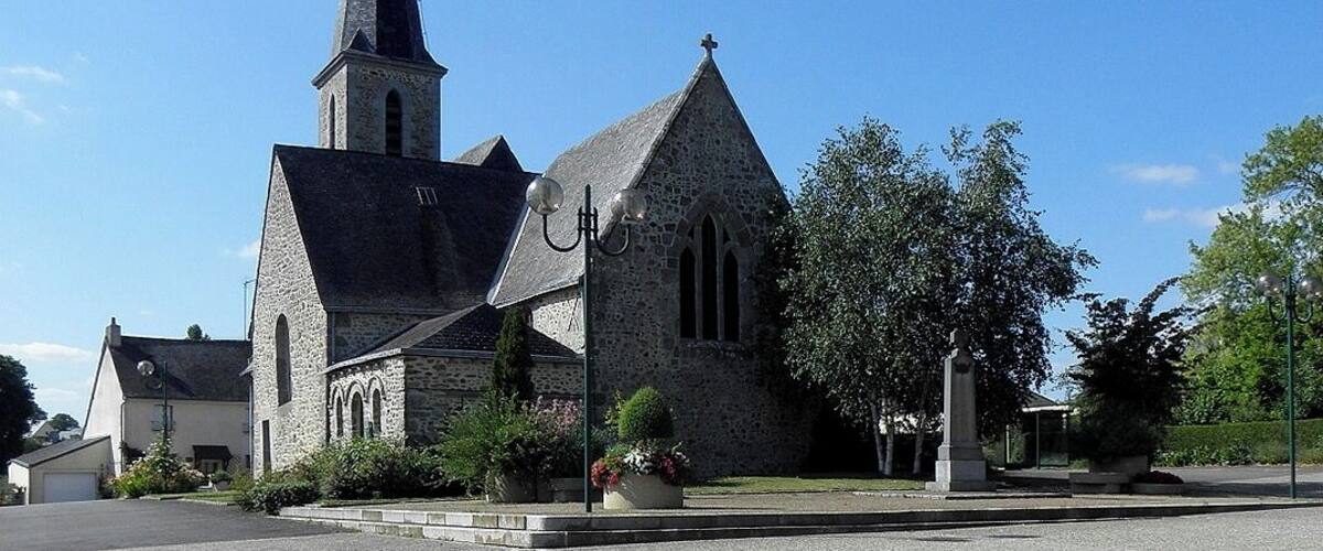 A church with a tall steeple and a cross on top, surrounded by greenery and a clear blue sky.