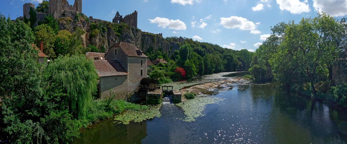 A historic castle on a hill, a river with lily pads, and lush greenery.