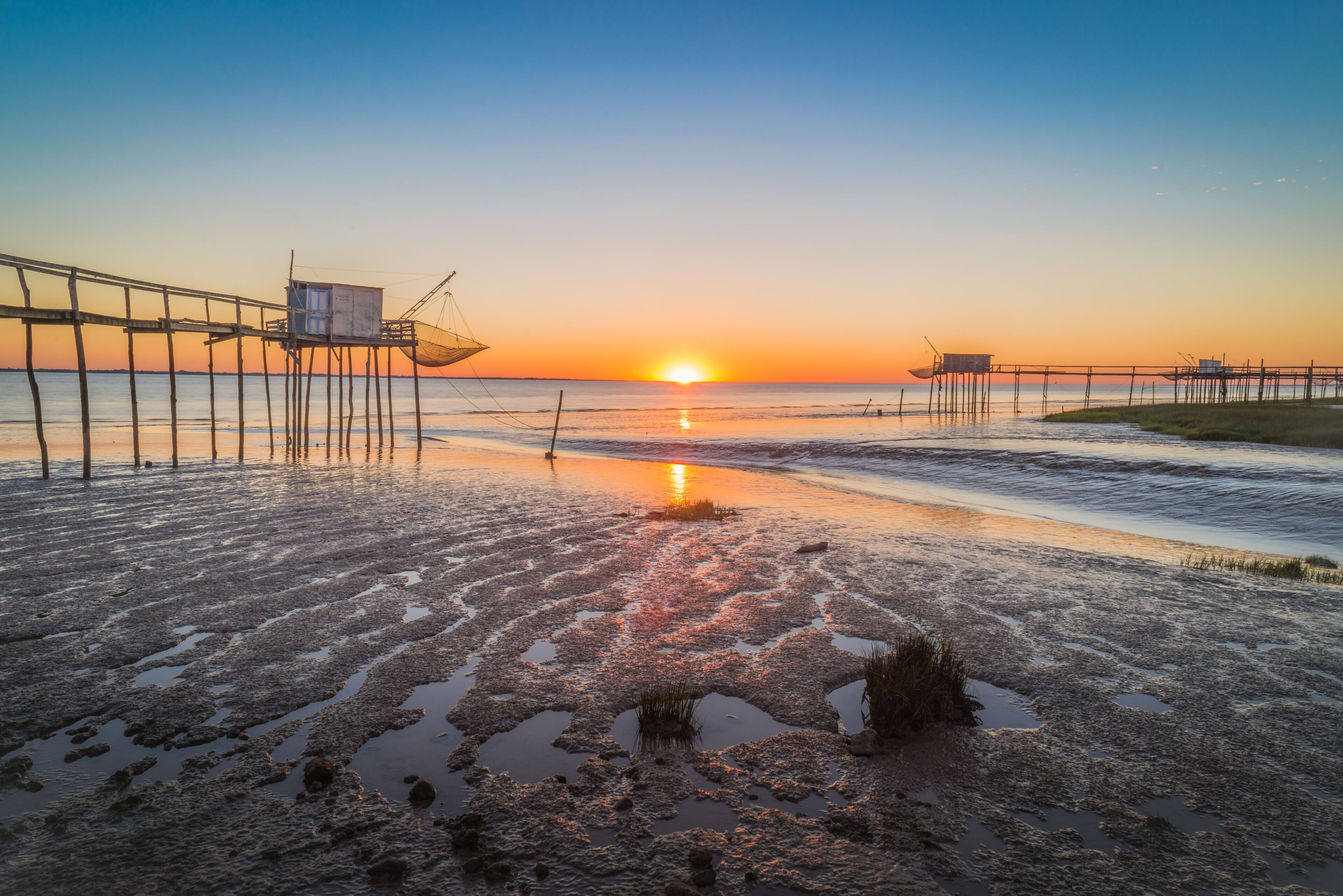 A beach with a pier extending into the water during sunset.