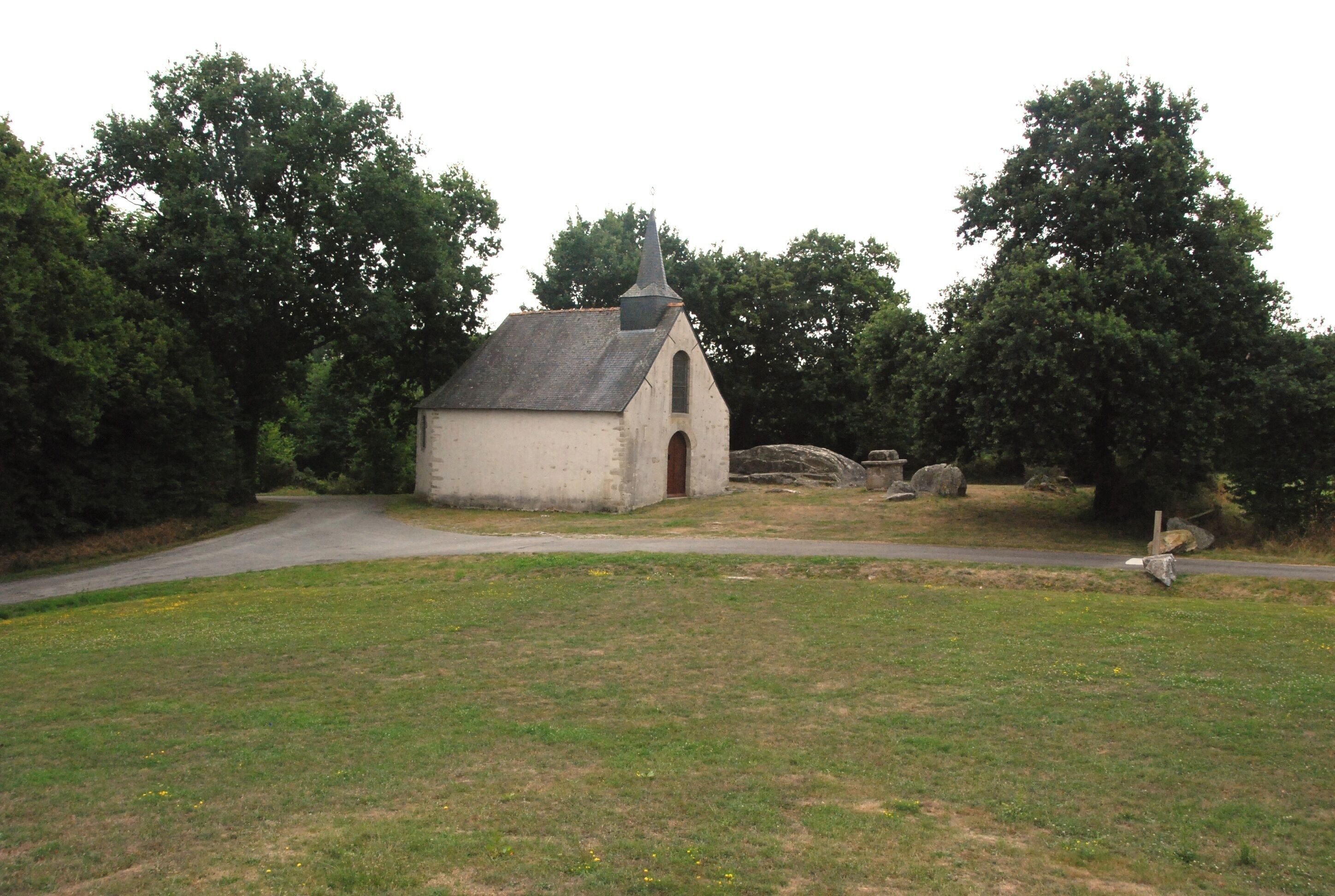 A small church with a pointed steeple surrounded by trees and a grassy field.