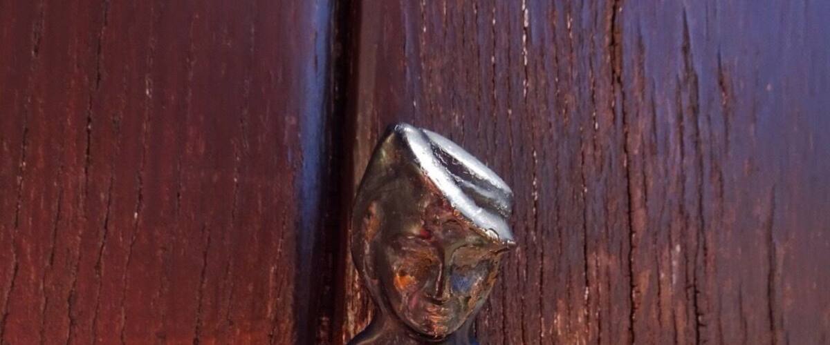 A small, dark-colored figurine with a shiny top, placed on a light-colored surface against a wooden background.