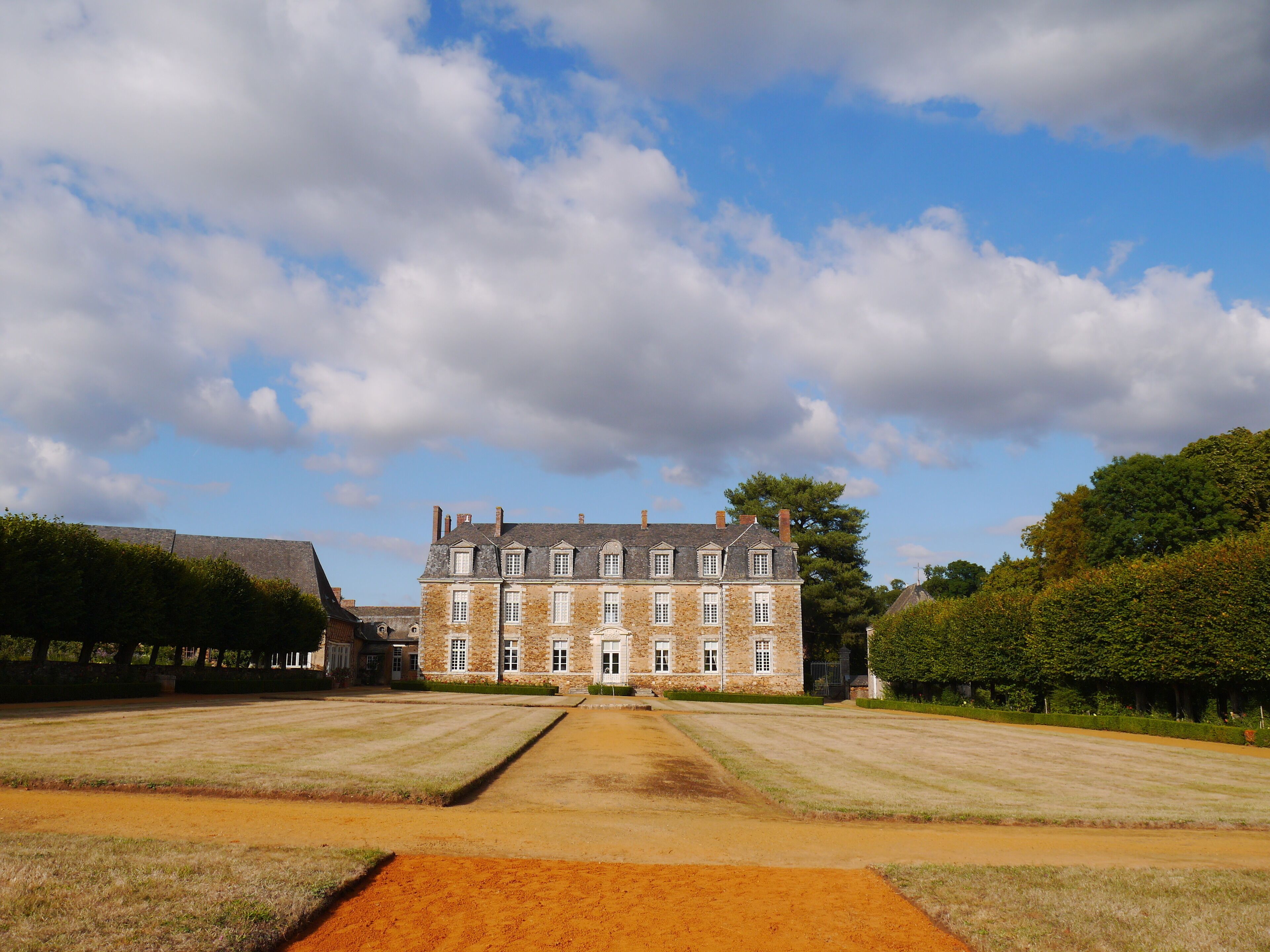 A large stone building with a symmetrical facade, surrounded by a well-maintained lawn and hedges.